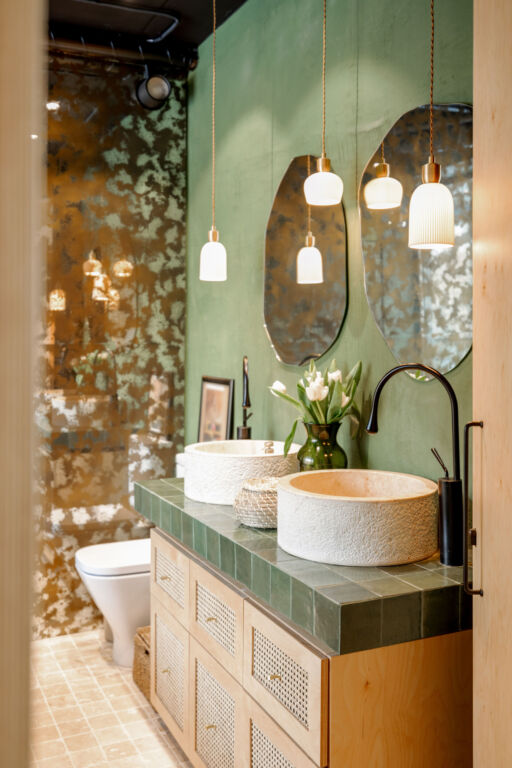 Bathroom interior with stone wash basins, modern faucets, irregularly shaped mirrors and wooden rattan commode in green and beige tones in natural boho style