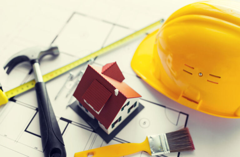 architecture, building, construction, real estate and home concept - close up of living house model on blueprint with repair tools