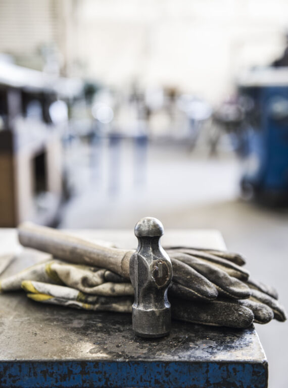 Closeup still life of gloves and a heavy duty hammer in a sheet metal factory.