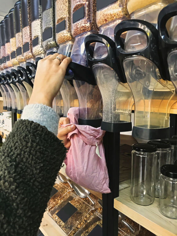 Hipster girl filling her reusable bag with groceries, shopping in bulk store with no waste. Support Local small business. Zero waste shopping. Plastic free marketplace