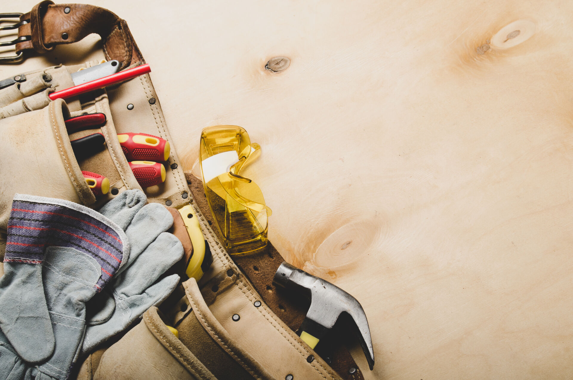 Tool belt with carpenter tools and protective wear on plywood sheet flat lay view